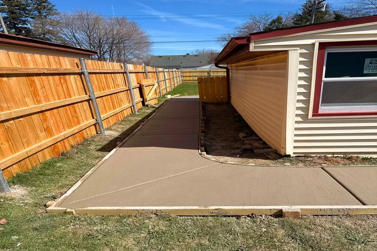 Wood fence lining a fresh concrete walkway between two properties